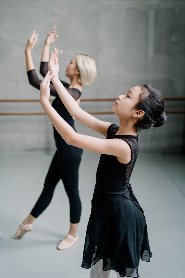 Side view Asian woman and girl ballerinas in black wear dancing ballet with arms raised in spacious light studio