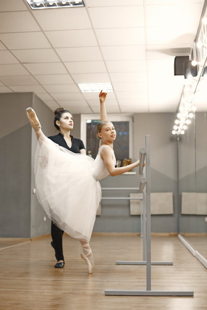 Young ballerina learns at the ballet bar with teacher in studio.
